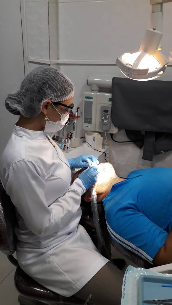Dra. Israela Lins durante atendimento odontológico em consultório, com paramentação completa e lupas de magnificação