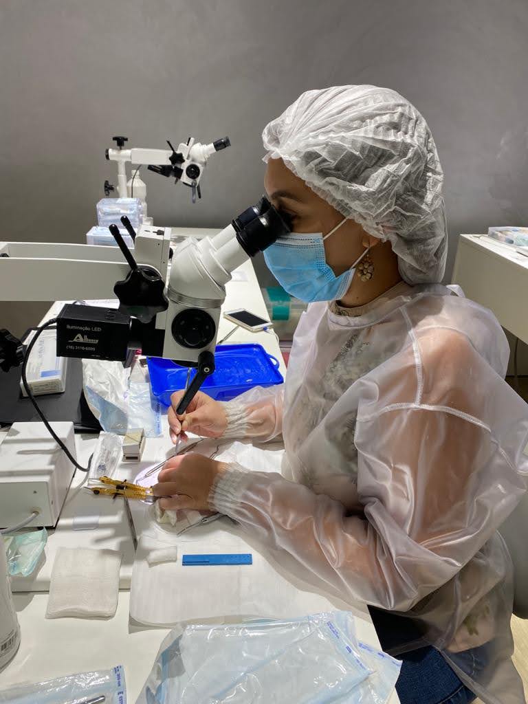 Dra. Israela Lins em atividade de pesquisa laboratorial, utilizando microscópio odontológico